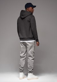 Donkergrijze hoodie met een trekkoord, grijze cargobroek en witte sneakers. Een marineblauwe pet maakt de outfit compleet. Subtiele texturen op de materialen.