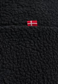 Svart fleece-material med en texturerad, plyschyta och en liten röd och vit dansk flagga som är sydd i det.