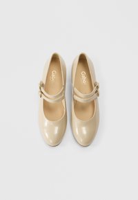 Beige Mary Jane-sko i laklæder med rundet tå, dekorative spænderemmes and en glat, blank finish.