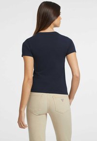 Camiseta ajustada azul marino de manga corta, con escote redondo y suave tejido de algodón, combinada con jeans beige claros que tienen bolsillos traseros.