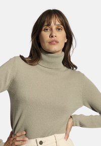 Pull colletto alto grigio chiaro in materiale a costine, con maniche lunghe e design aderente, abbinato a pantaloni cream a vita alta.