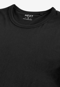 T-shirt nera in cotone con collo a giro, caratterizzata da una texture liscia e un'etichetta stampata con la scritta "NEXT M" all'interno del colletto.