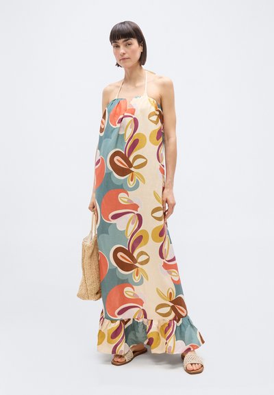 Γυναίκα που φοράει πολύχρωμο μακρύ φόρεμα με halter λαιμόκοψη και αφηρημένα λουλουδένια σχέδια, κρατώντας πλεγμένη τσάντα tote και φορώντας πλεγμένα σανδάλια.