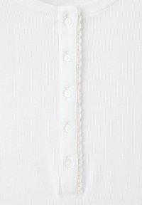 Tissu blanc côtelé avec une rangée verticale de cinq petits boutons blancs et une délicate bordure en dentelle le long d'un côté.