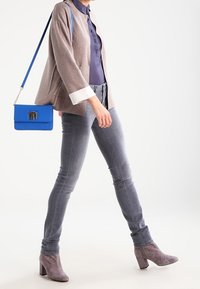 Světle hnědá bunda s bílými manžetami, modrá blůza, šedé skinny džíny a šedé kotníkové boty. Modrá kabelka s kovovým západkou.