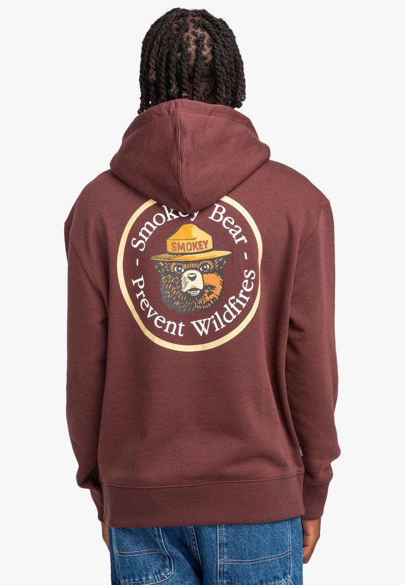 Felpa bordeaux con cappuccio, caratterizzata da una grande grafica circolare di Smokey Bear sul retro. Il materiale sembra morbido, con polsini e orlo a coste.