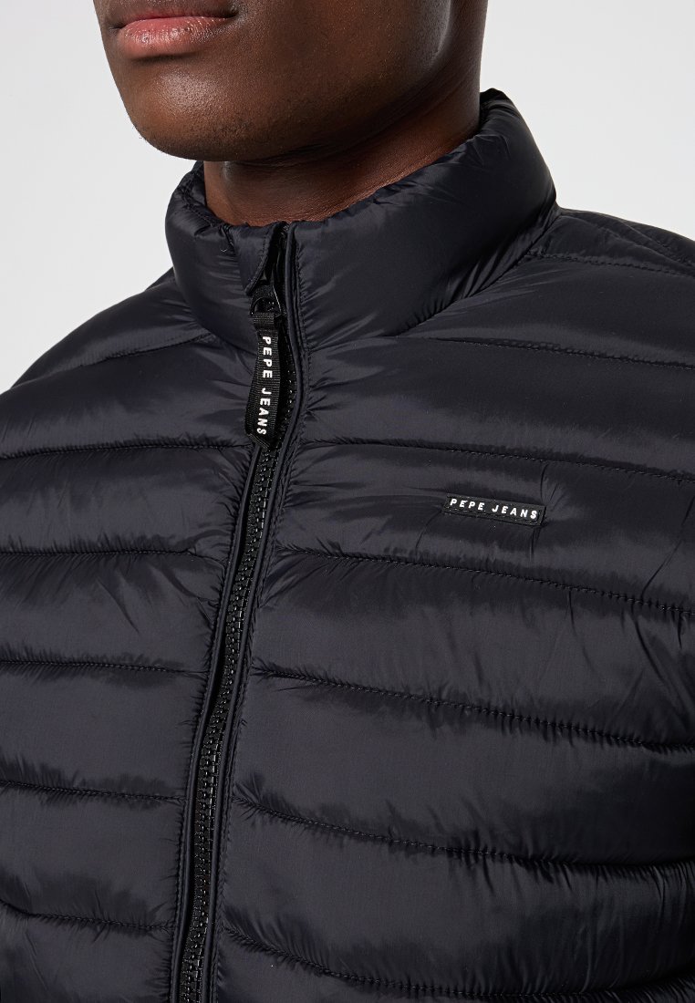 Doudoune noire avec un col haut, fermeture éclair, design matelassé et branding subtil. Texture lisse avec rembourrage isolant.