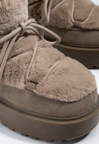 Fluweelachtige taupekleurige winterlaarzen met dikke zolen en bijpassende ronde veters gestrikt in een strik op zachte, pluche stoffen bovenzijde.