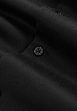 Crni materijal s glatkom teksturom sadrži dugme s četiri rupe na kojem je urezana riječ "REISS". Ukupni dizajn je pojednostavljen i minimalistički.
