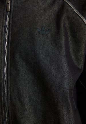 Casaco preto com fecho éclair, feito de um tecido texturizado. Apresenta um logo escuro discreto e costuras em contraste ao longo das costuras.