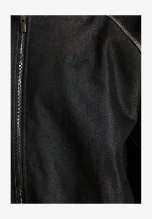 Giacca nera con zip realizzata in tessuto testurizzato. Presenta un logo scuro e discreto e cuciture a contrasto lungo le cuciture.