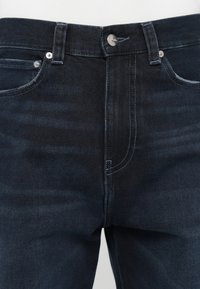 Dark blue denim jeans featuring a classic five-pocket design, visible stitching, and a metal button closure at the waistband.
