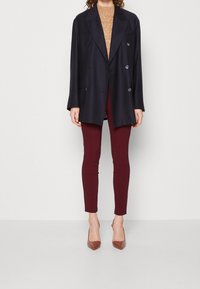 Marinblå dubbelknäppt kavaj över en beige tröja, i kombination med vinröda tajta byxor och bruna högklackade skor, med en slät textur.