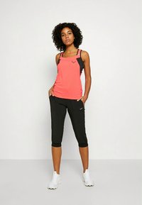 Top desportivo em coral vibrante com alças pretas, combinado com leggings capri pretas. Calçado são ténis desportivos brancos.