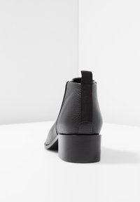 Schwarze Leder-Ankle-Boots mit strukturiertem Finish, quadrater Zehenform, elastischem Seiteneinsatz und niedrigem Blockabsatz.