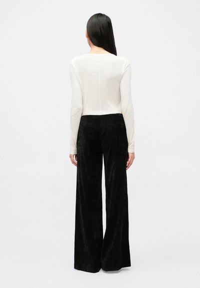 Haut crème à manches longues avec encolure dégagée, associé à un pantalon noir en velours côtelé à taille haute et jambes larges, mettant en valeur une surface texturée.