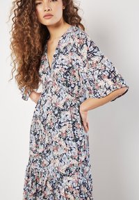 Kleid mit Blumenmuster, tiefem V-Ausschnitt, lockeren Ärmeln und gestuftem Saum. Es hat einen dunkelblauen Hintergrund mit rosa, blauen und grünen Blumenmustern.