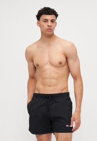 Shorts de bain noirs avec une taille élastique et un cordon de serrage, ornés d'un petit logo brodé en bas à droite.