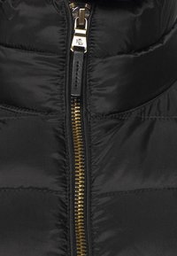 Svart vadderad jacka med gyllene metallblixtlås och läderdragflik präglad med "RL" initialer.