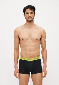 Sorte boxershorts med en gul livrem med merkevarenavnet "PUMA" i fet tekst. Glatt stoff og tettsittende design.