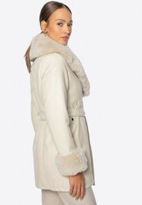 Kremowy płaszcz z futrzanym kołnierzem i mankietami, w talii, z długimi rękawami i gładkim wykończeniem, wyeksponowany w widoku bocznym.