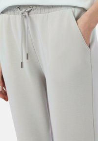 Hellgraue Jogginghosen mit elastischem Bund, verstellbarem Kordelzug und seitlichen Taschen; glattes Material mit weicher Textur.