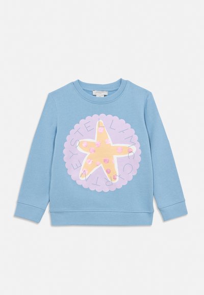 Sinine pikkade varrukatega dressipluus, millel on suur kollane meritäht ja roosad täpid lavendlivärvilise lainelise ringi sees ning ümberringi tekst.