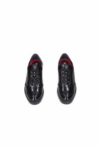 Zapatillas de charol negro con un acabado texturizado, que presentan una puntera redondeada, un cuello acolchado y cordones negros sobre un forro interior rojo.