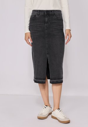 Jupe midi en denim noir avec une fente avant, un ourlet brut et un design à cinq poches. Associée à des baskets blanches et un haut léger à manches longues.