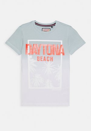 Hellblaues kurzärmeliges T-Shirt mit der Aufschrift „DAYTONA BEACH“ in kräftigem Orangeton und einem weißen, rechteckigen Rahmen, in dem schwache Palmenmotive zu sehen sind.