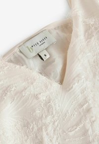 Rochie roz deschis cu țesătură texturată, având un decolteu în V și accente suprapuse cu franjuri. Eticheta spune "By Ted Baker, London," mărimea 8.