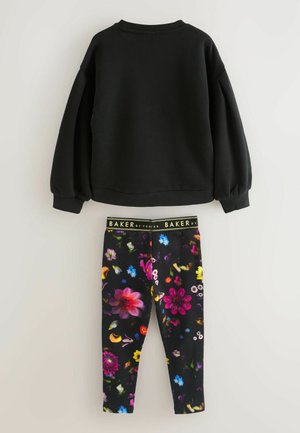 Schwarzes Sweatshirt mit Puffärmeln, kombiniert mit schwarzen Leggings, die mit einem bunten Blumenmuster und einem elastischen, markierten Bund versehen sind.