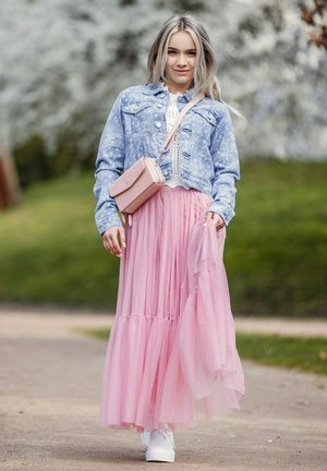 Light blue denim jacket, white knit top, flowing pink tulle skirt, and white sneakers. Small pink crossbody bag. Green background.