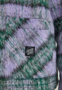 Fuzzy jacket featuring a blend of purple and green fibers, with a front pocket and a black "Santa Cruz" logo patch.