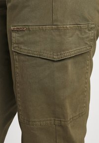 Calças cargo de cor verde-oliva com um acabamento texturizado, apresentando um bolso com aba e detalhes de costura discretos. Tecido durável com um design casual.