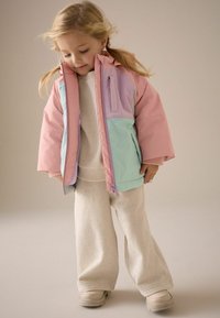 Pastellfärgad pufferjacka med paneler i rosa, lavendel och mint; med dragkedjefickor; bärs över en ljuskrämig texturerad topp och träningsbyxor.