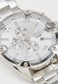 Reloj de acero inoxidable plateado con una esfera redonda texturizada, tres subesferas y una pantalla de fecha. Cuenta con marcadores de hora en negrita y una pulsera vinculada.