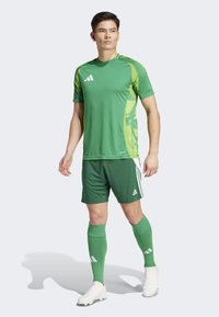 Green athletic jersey with light green accents, matching green shorts, and socks. Features Adidas logo and a textured design on the shirt.