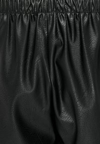 Tela de piel sintética negra con una textura suave, que presenta una cinturilla fruncida y pliegues visibles, indicando un diseño drapeado.