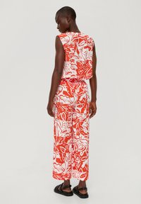 Czerwono-biały kombinezon we wzory z bezrękawym topem i szerokimi spodniami. Wykonany z lekkiej tkaniny, z liściastym wzorem. Czarne sandały.
