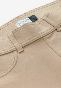 Béžové legíny z jersey materiálu s hladkým texturem, s prošitým pasem a štítkem s nápisem "Celkové legíny Jersey."