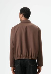 Bruine bomberjack met een rechte snit, elastische tailleband en lange mouwen. Glad stoffen textuur met een klassieke kraag.