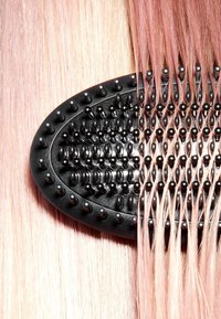 Zwarte haarborstel met gladde, rechte, roze getinte haarlokken netjes gerangschikt over de borstelharen.