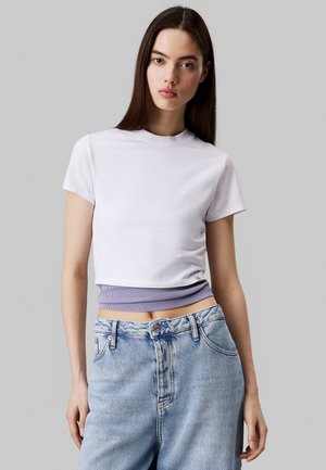 T-shirt bianco a maniche corte con orlo a coste lilla. Abbinato a jeans in denim chiaro a vita alta.