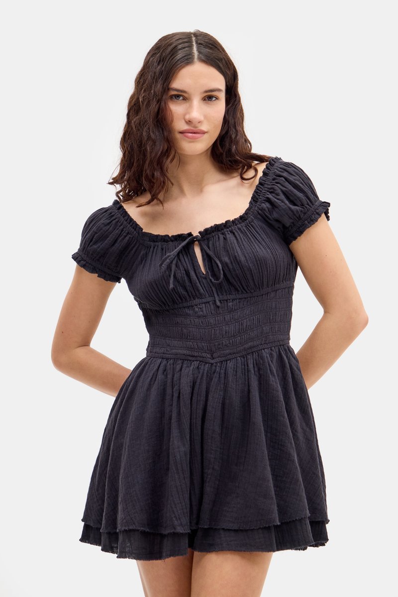 Robe noire avec des manches bouffantes courtes, un corsage froncé, un détail en trou de serrure à l'avant et une jupe superposée. Fabriquée en tissu texturé.