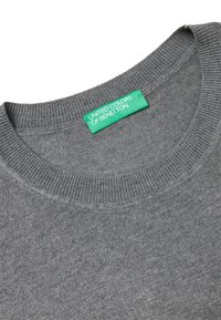 Šedý svetr s žebrovaným výstřihem a zelenou cedulkou s nápisem "United Colors of Benetton." Materiál má hladkou, jednotnou texturu.
