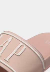 Sandale à glissière rose avec des lettres blanches en relief formant le mot "GAP" sur la bride au-dessus du pied.