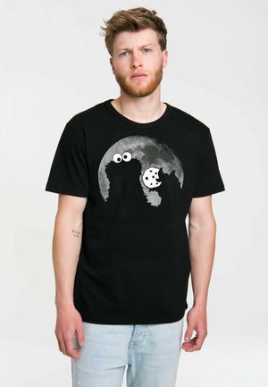 Camiseta negra de manga corta con un gráfico de una galleta y un monstruo sobre un diseño de luna gris, hecha de suave tejido de algodón.