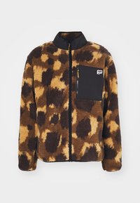 Chaqueta de forro polar marrón con manchas negras, con cremallera completa y bolsillo en el pecho con cremallera negra que lleva el logo de Puma.