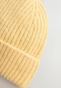 Nertas geltonas šalikėlis su raštu, pagamintas iš minkštos, pūstaus audinio, kuris gerai priglunda.